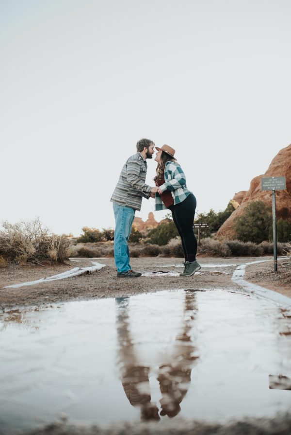 Couple kissing during an adventurous outdoor couples photoshoot in the Utah desert with reflection in water.