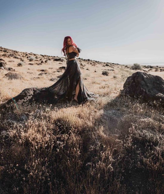 woman in a blue dress standing in sagebrush and rocks