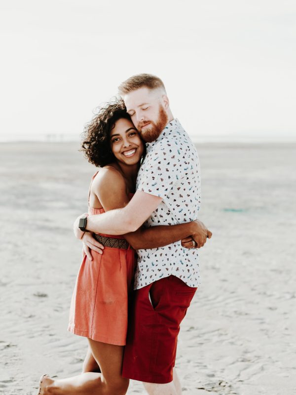 Couple hugging during a romantic beach engagement photoshoot at sunset.