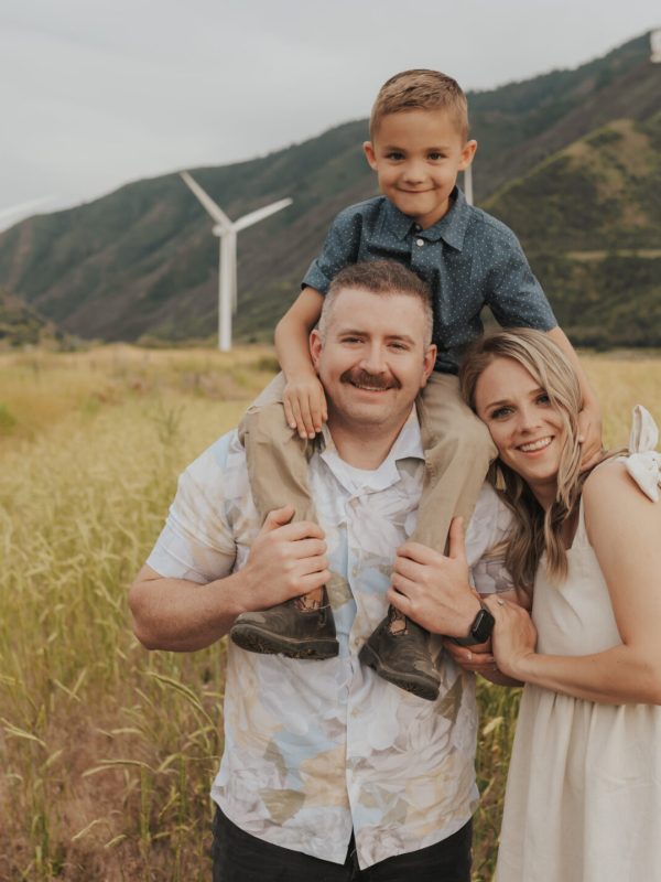 Family standing together during an outdoor lifestyle family photoshoot with turbines in the background at sunset.