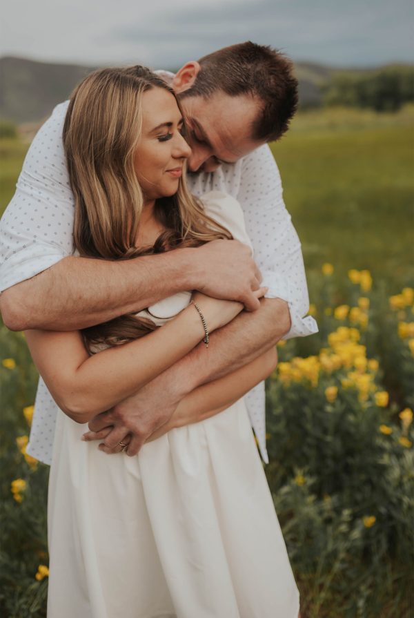 Romantic couples photoshoot in a mountain field featuring a couple kissing surrounded by yellow wildflowers.