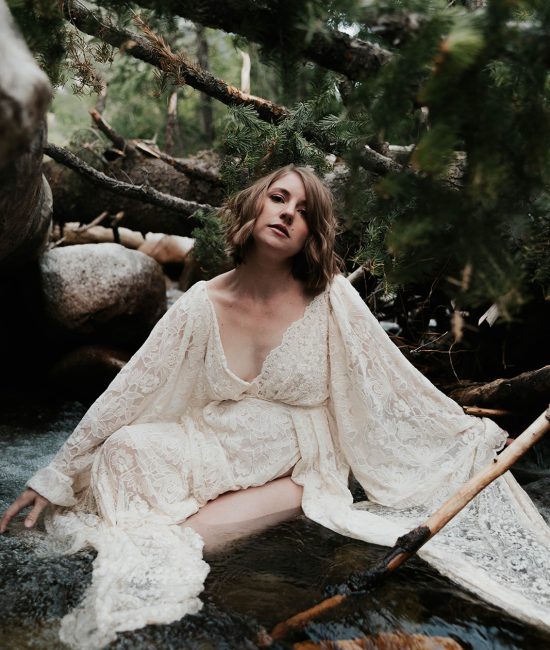 Woman in a white dress sitting in a river in the middle of a forest