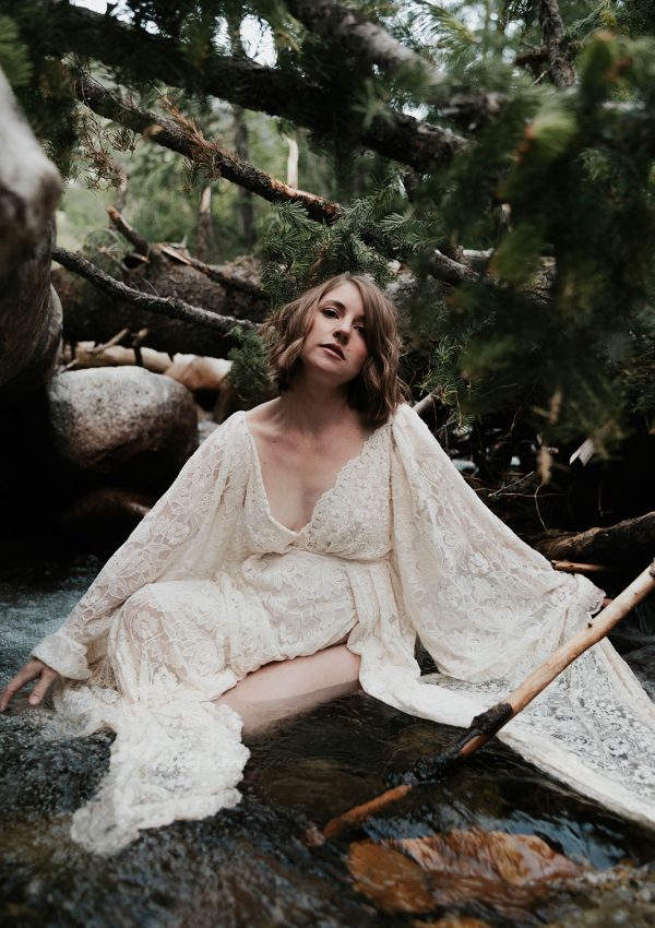Woman in a white dress sitting in a river in the middle of a forest