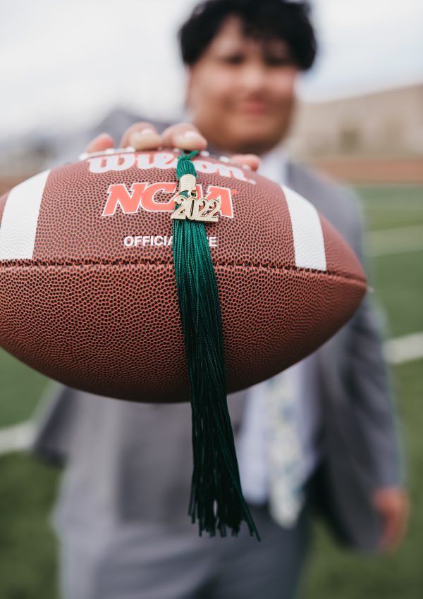 High school senior holding a football with a 2022 graduation tassel during a creative senior portrait session on a football field.